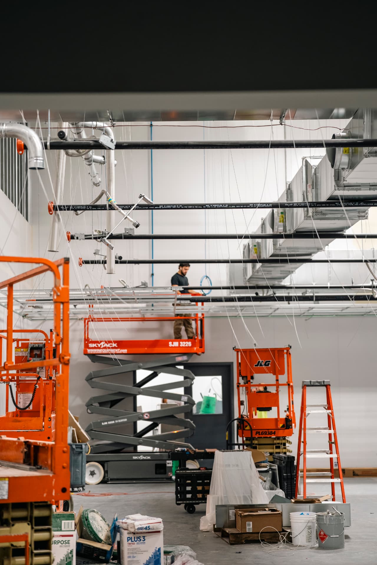 Active commercial construction site with overhead ductwork, sprinkler mains and ceiling grid in progress
